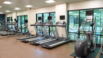 A gym with multiple treadmills and exercise bikes, large windows, and a view of the outdoors.