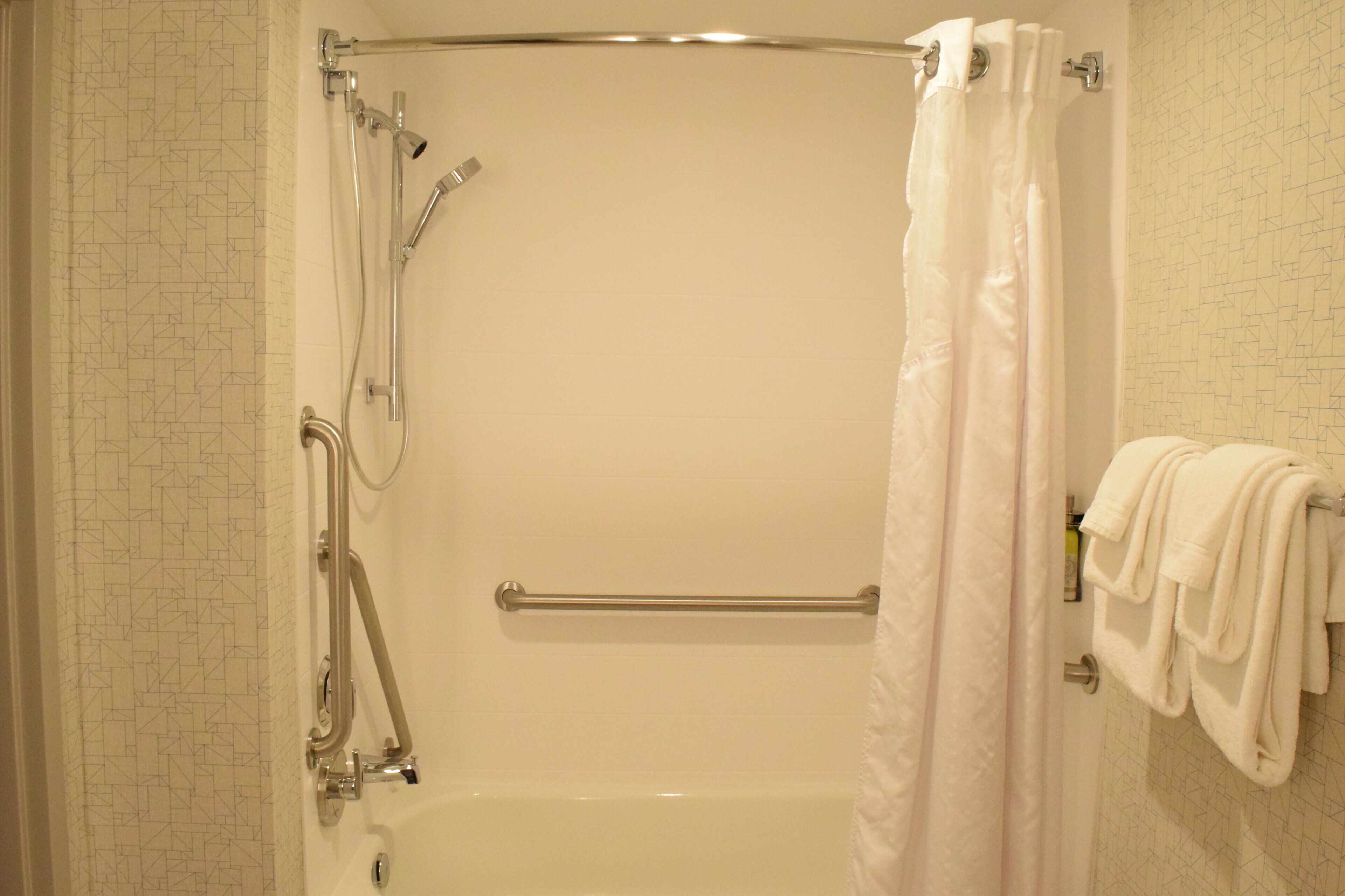 Ein Badezimmer mit einer Badewanne, einer Dusche und Haltegriffen.