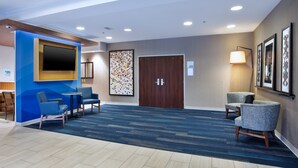 A hotel lobby with a blue accent wall, a flat-screen TV, a large abstract painting, a wooden door, and two seating areas with chairs. - Holiday Inn Express & Suites Rochester Webster by IHG (Webster)