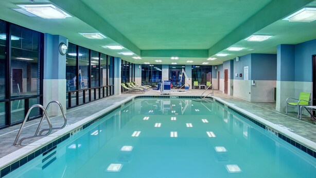 Une grande piscine intérieure avec des couloirs clairement délimités, entourée de chaises longues et dotée d’un espace vestiaire.