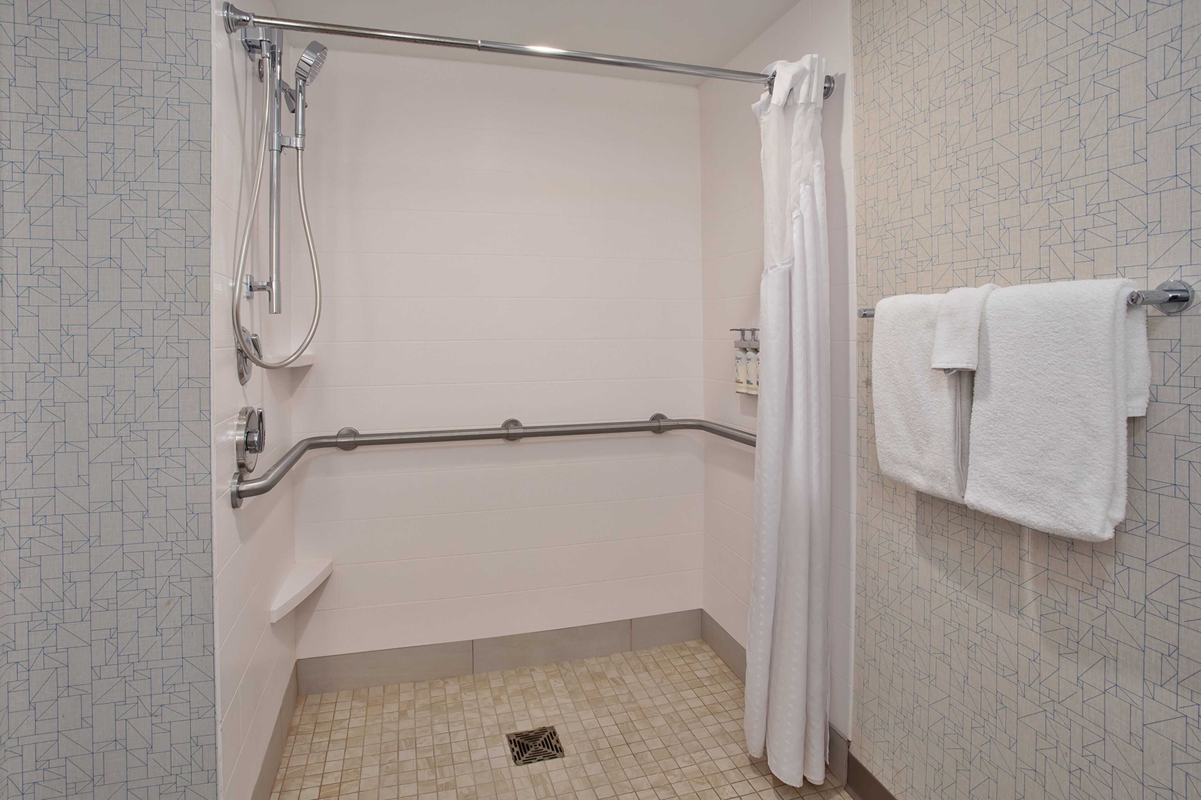 A shower with a grab bar, a white curtain, and a towel rack with two towels.