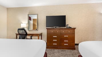 Quarto de hotel com duas camas, televisão, penteadeira, escrivaninha e espelho.