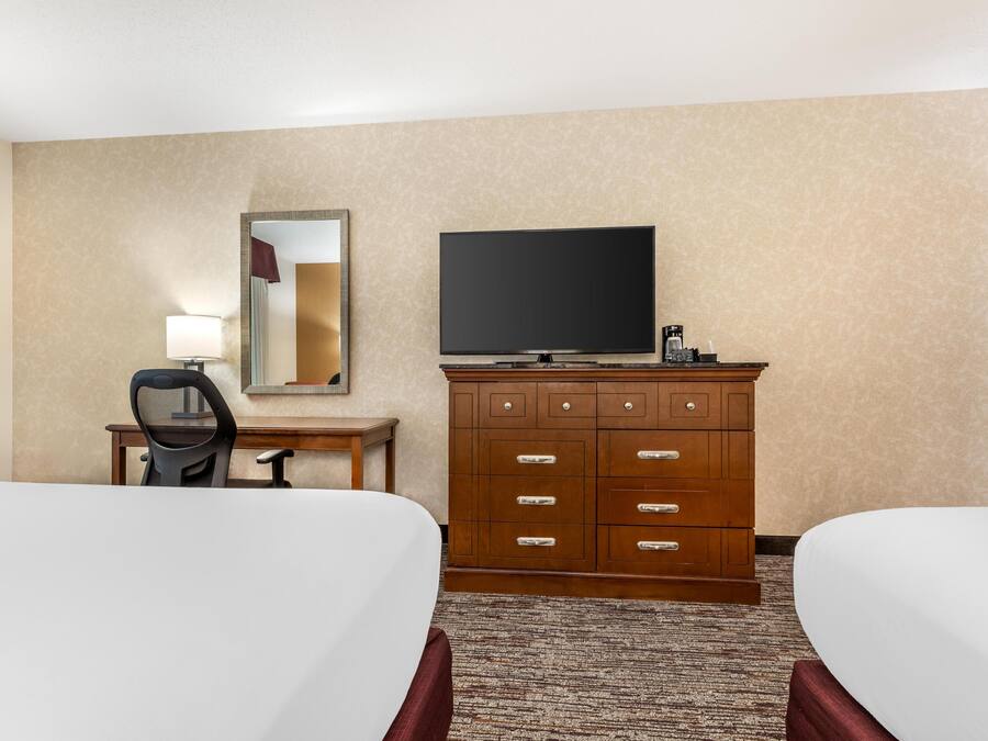 A hotel room with two beds, a TV, a dresser, a desk, and a mirror.