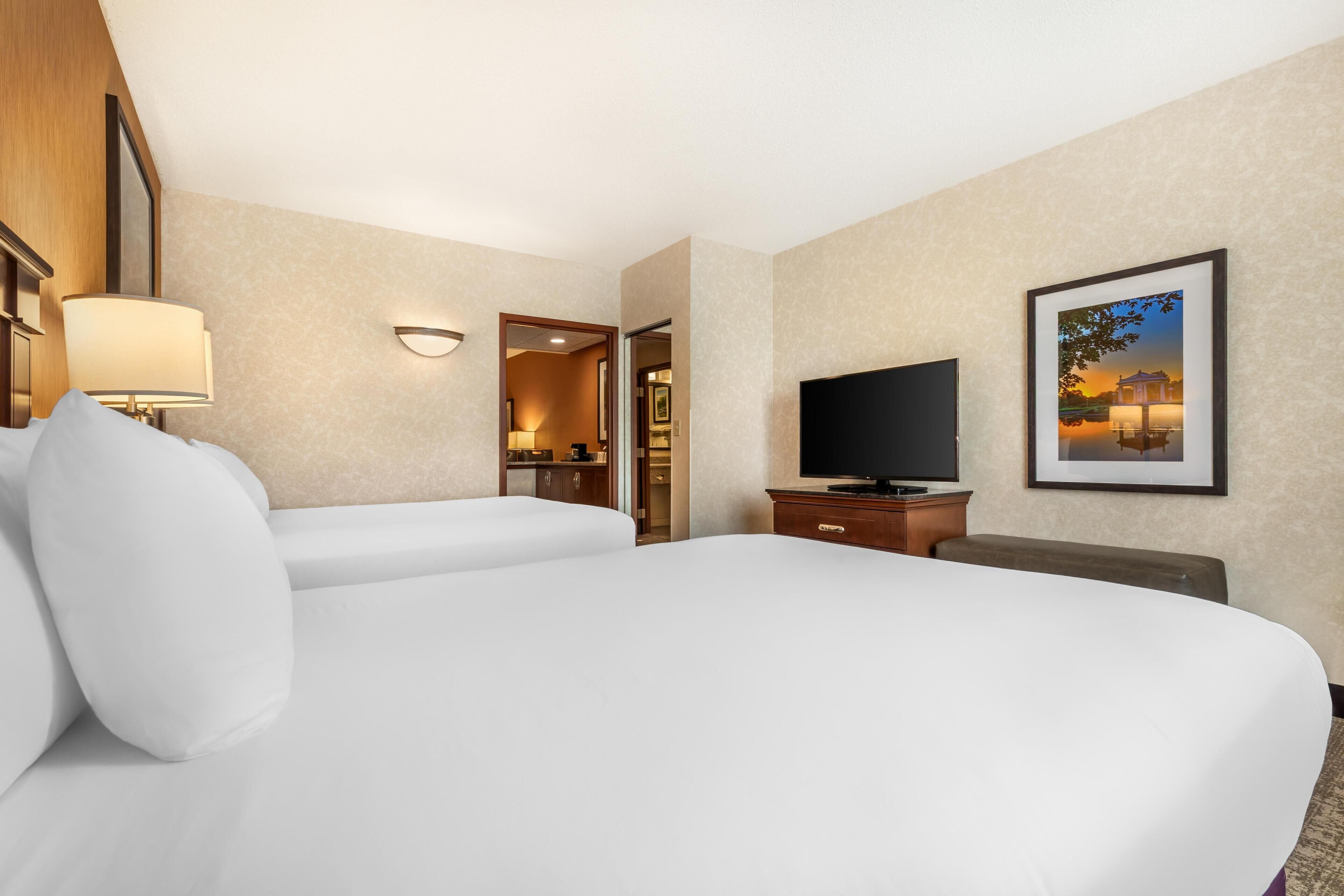 Quarto de hotel com uma cama grande, televisão, escrivaninha e um quadro na parede.