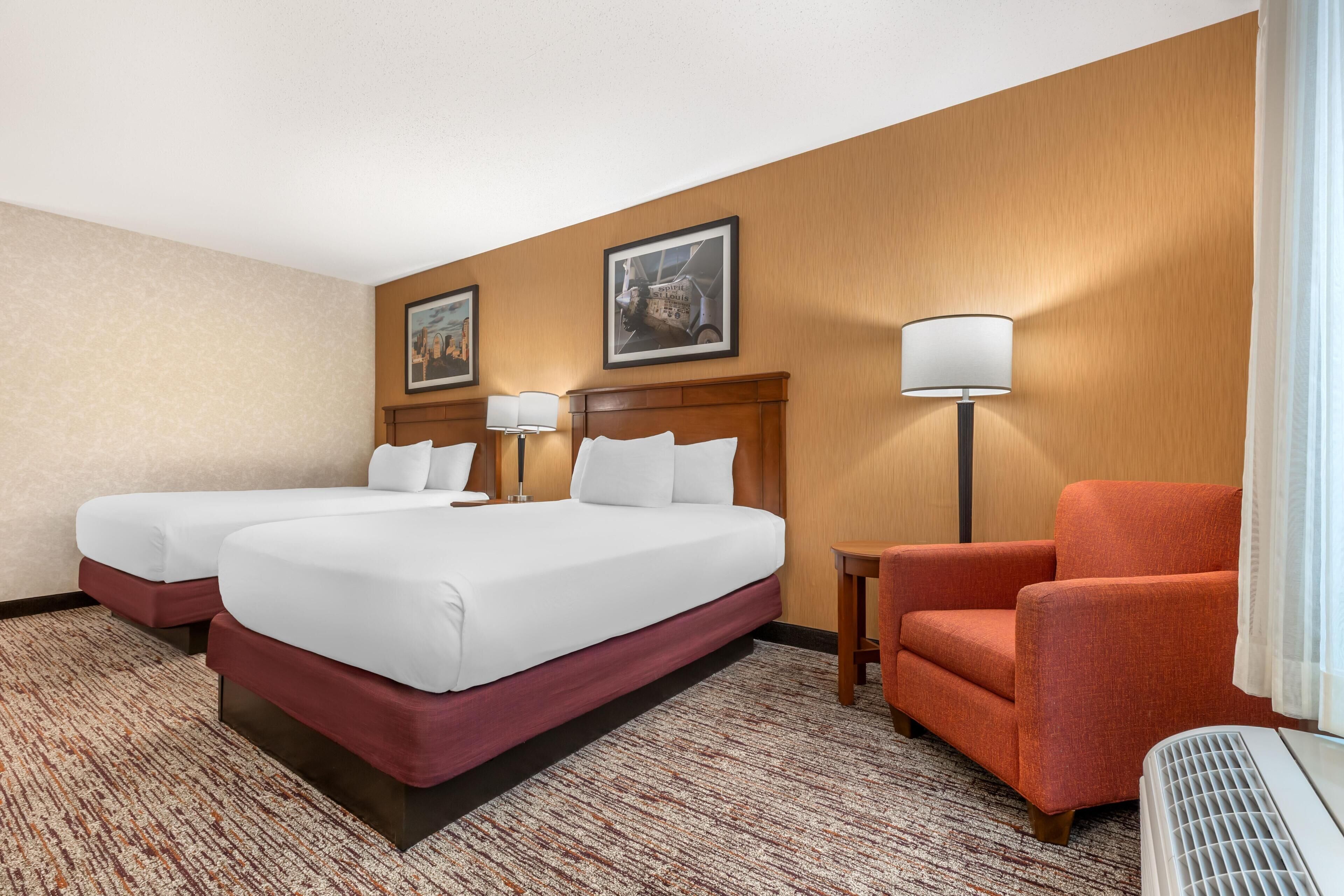 A hotel room with two beds, a chair, a lamp, and a heater.