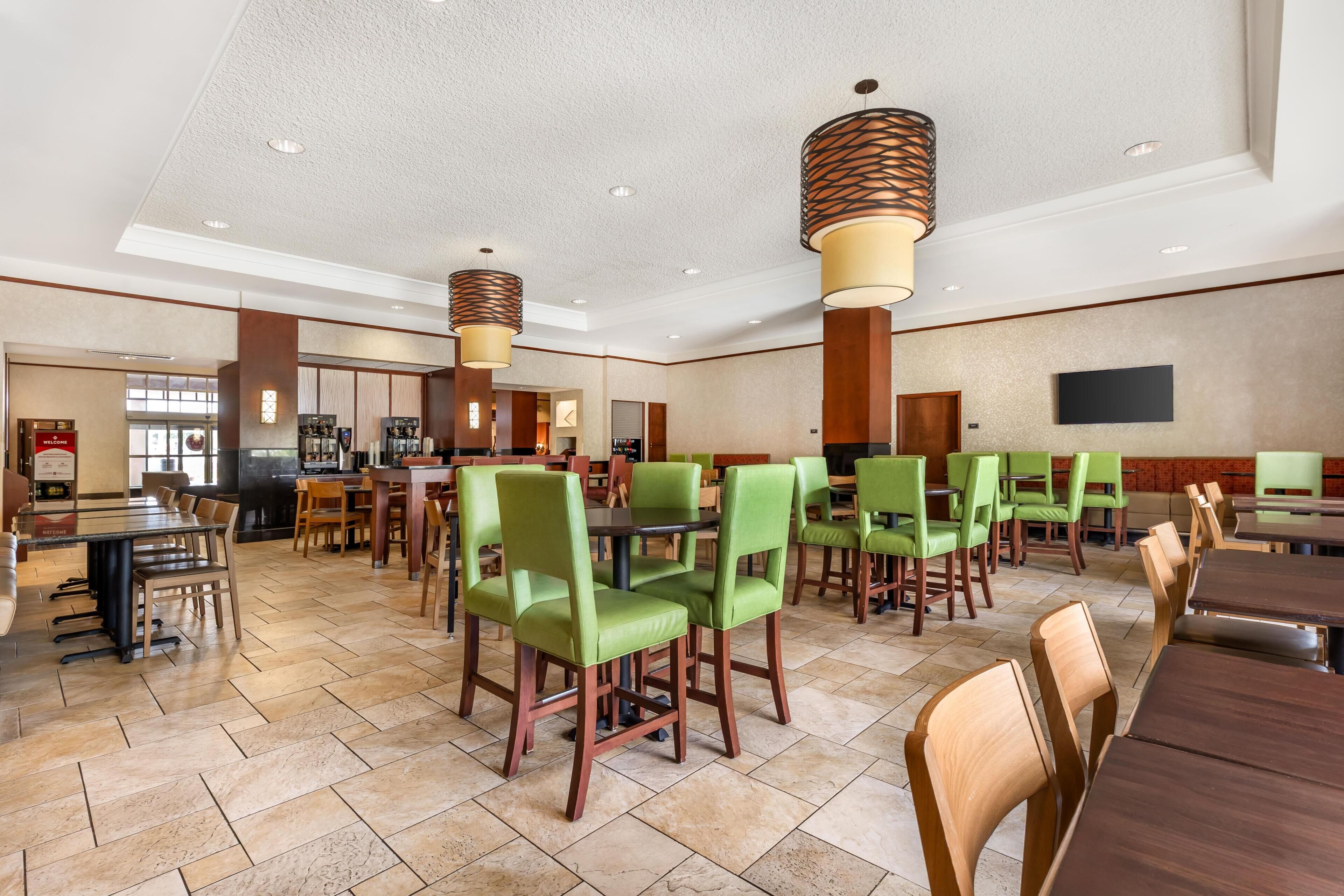 A spacious dining area with multiple tables and chairs, a kitchen area, and a flat-screen TV mounted on the wall.