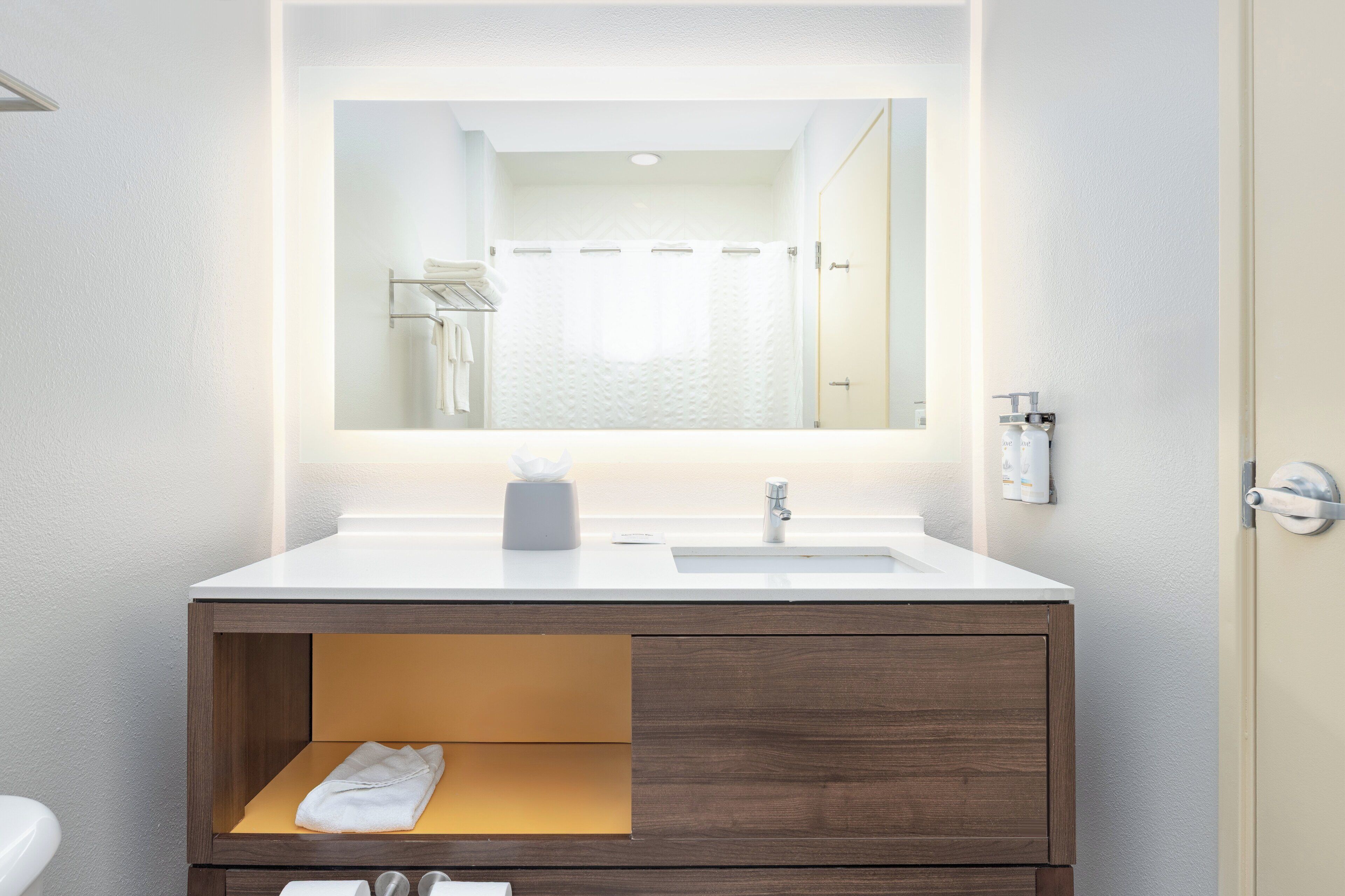 Un baño moderno con un lavamanos blanco, un espejo encima y un mueble de tocador de madera con un perchero.