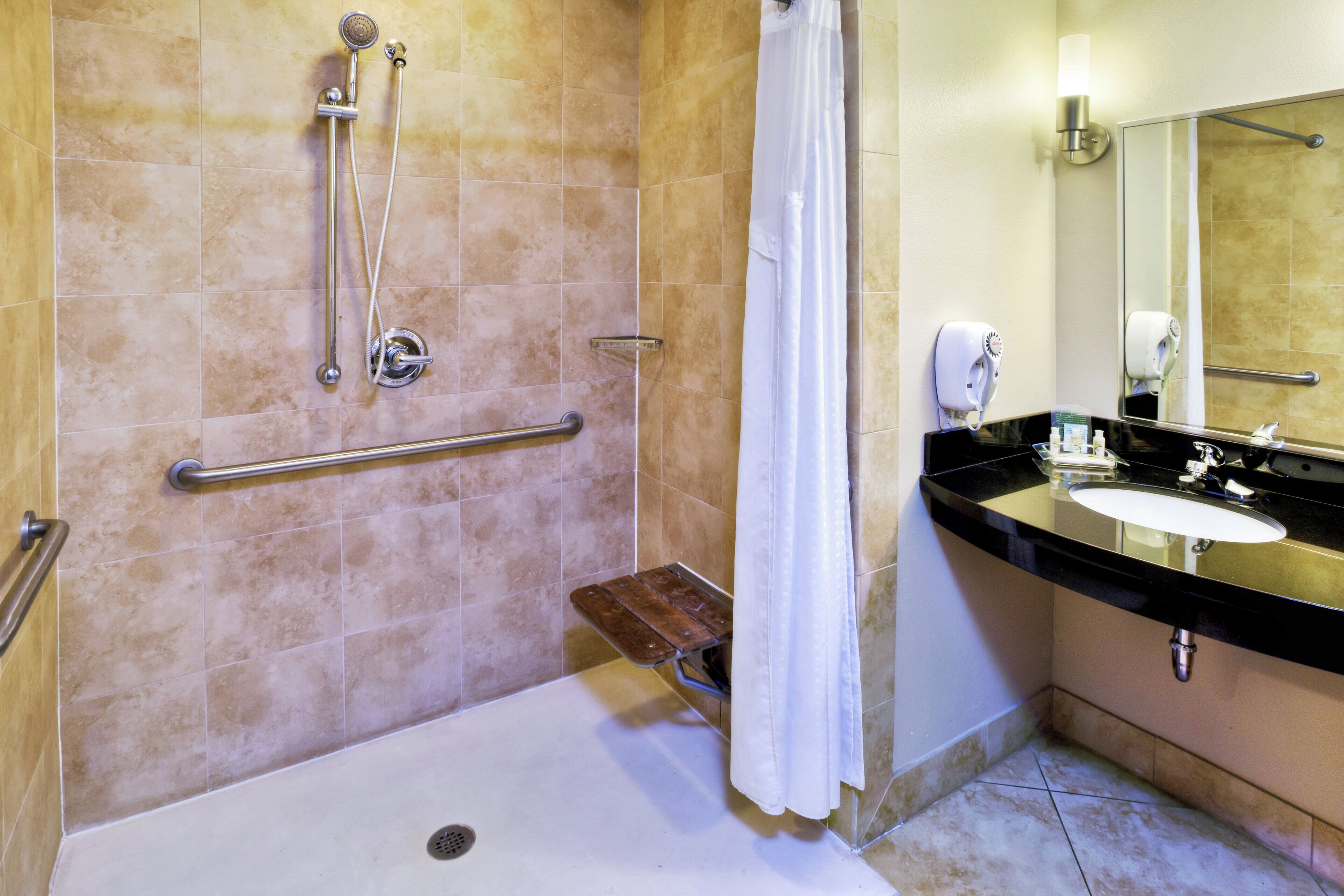 Baño con ducha, barra de apoyo, lavamanos y espejo.