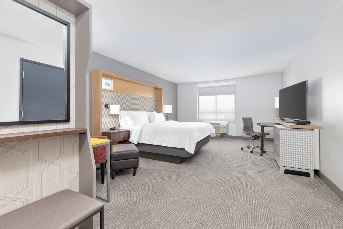 Ein modernes Hotelzimmer mit Bett, Schreibtisch, Stuhl und Fernseher.