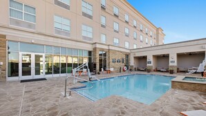 A hotel pool area with a stone-tiled deck, lounge chairs, and a building with large windows and a glass entrance. - Holiday Inn Killeen – Fort Hood Area by IHG (Killeen)