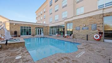 Een buitenzwembad, ligstoelen bij het zwembad