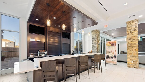 A modern bar area with a long counter, multiple bar stools, pendant lighting, and a stone accent wall. - Holiday Inn Killeen – Fort Hood Area by IHG (Killeen)