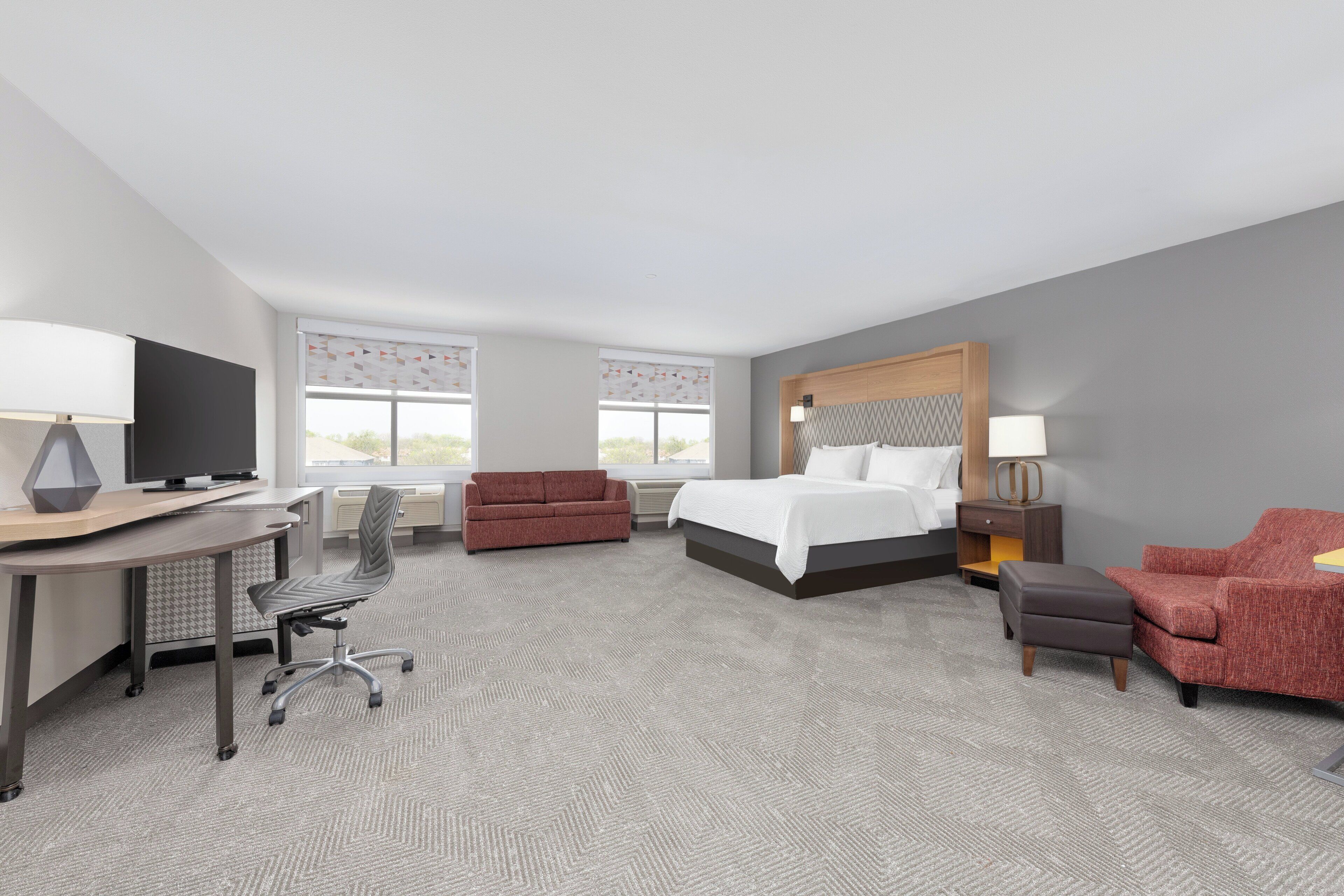 Una habitación de hotel con cama, escritorio, silla, sofá y televisor.