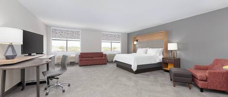 Una habitación de hotel con cama, escritorio, silla, sofá y televisor.
