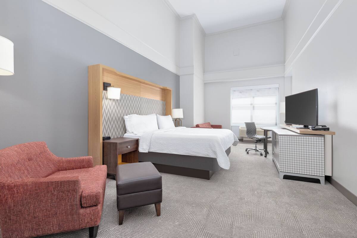Ein Hotelzimmer mit Bett, Schreibtisch, Fernseher, Stuhl und einem kleinen Tisch.