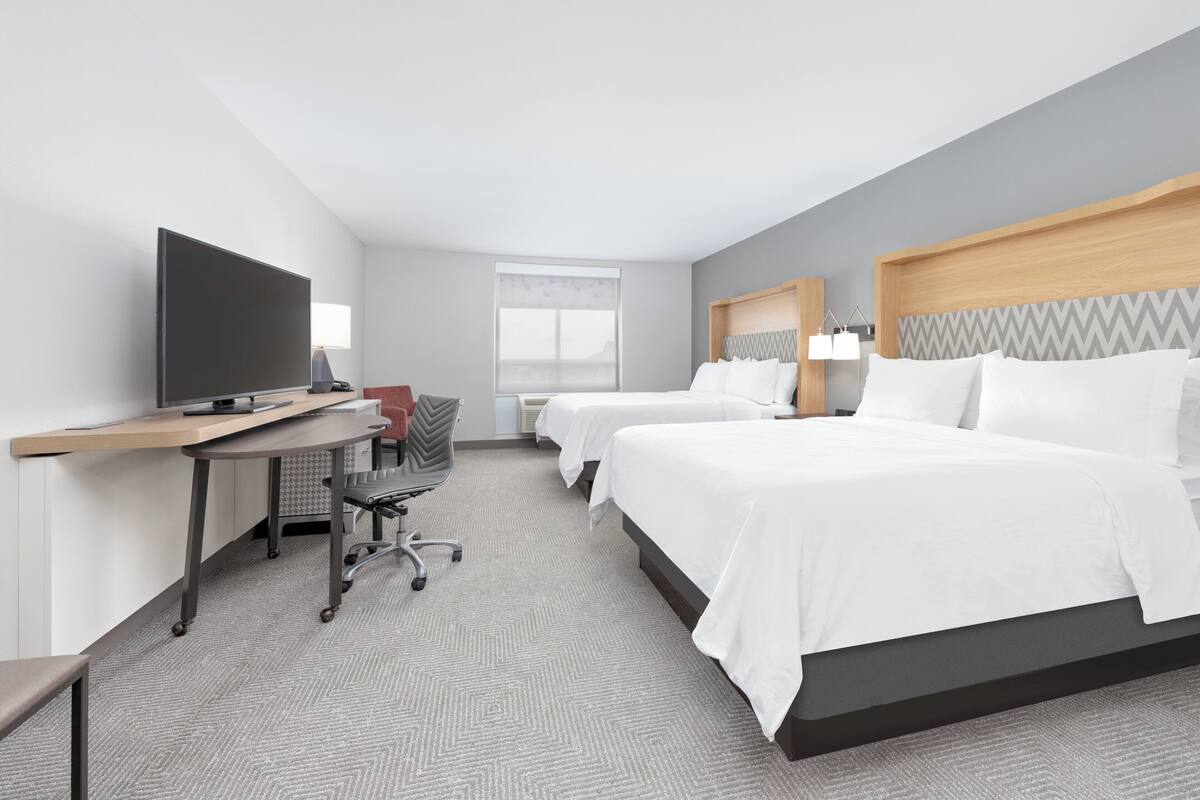 Ein Hotelzimmer mit zwei Betten, einem Schreibtisch mit Fernseher und einem Sessel.