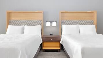 Habitación de hotel con dos camas, una mesita de noche con lámpara y una alfombra estampada.