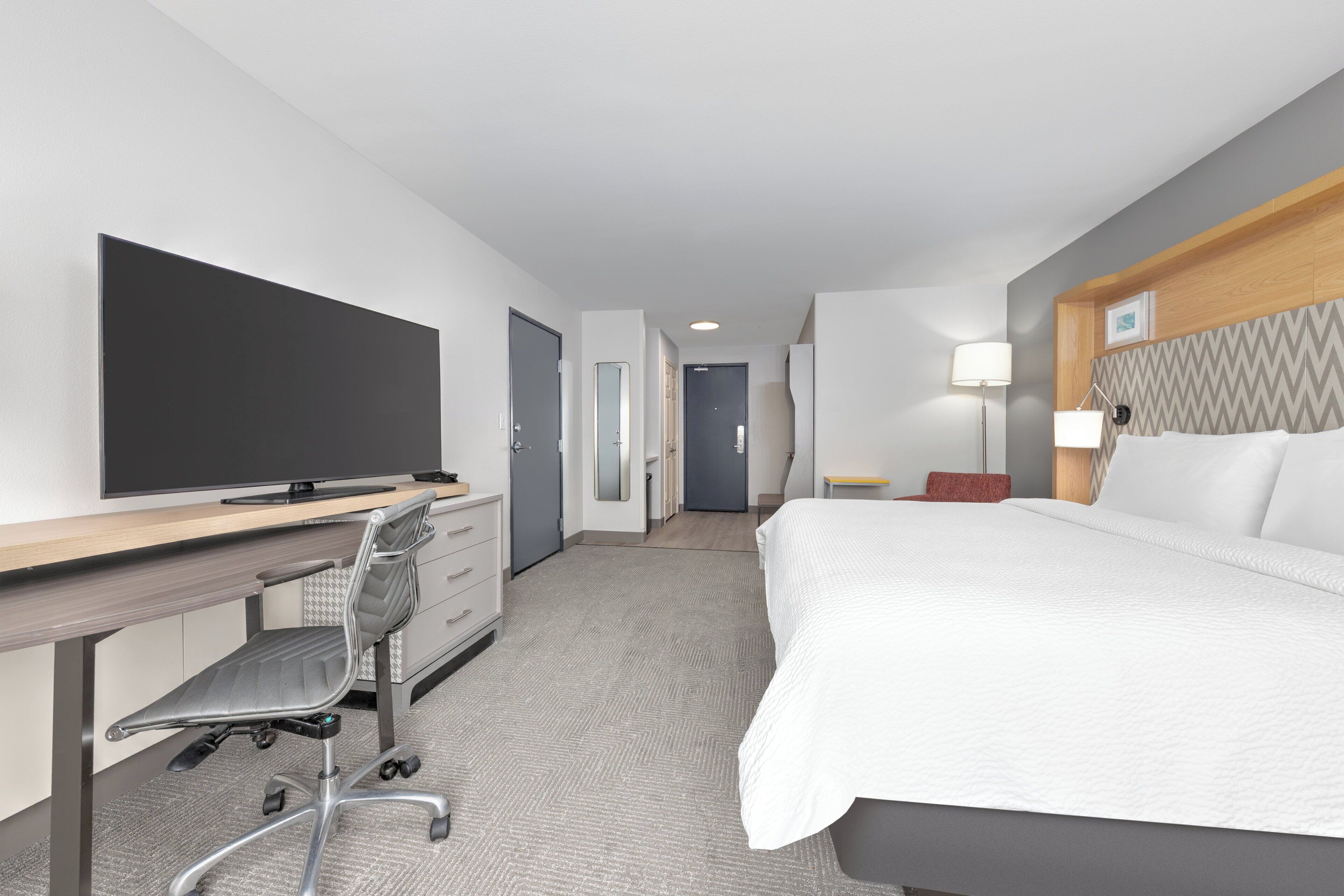 A hotel room with a bed, desk, chair, television, and a door leading to a bathroom.