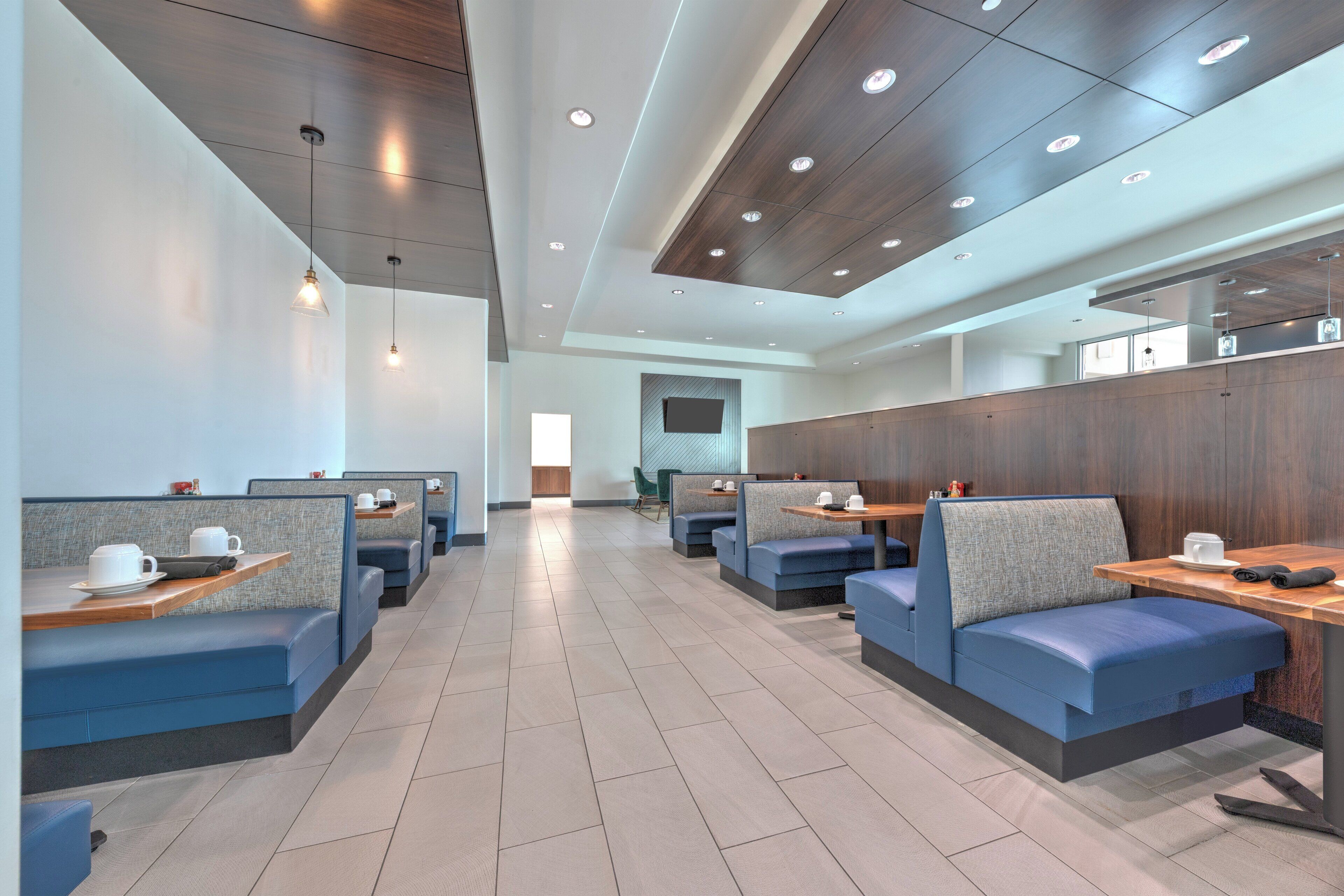 A modern restaurant with booths and tables, wooden ceiling, and recessed lighting.