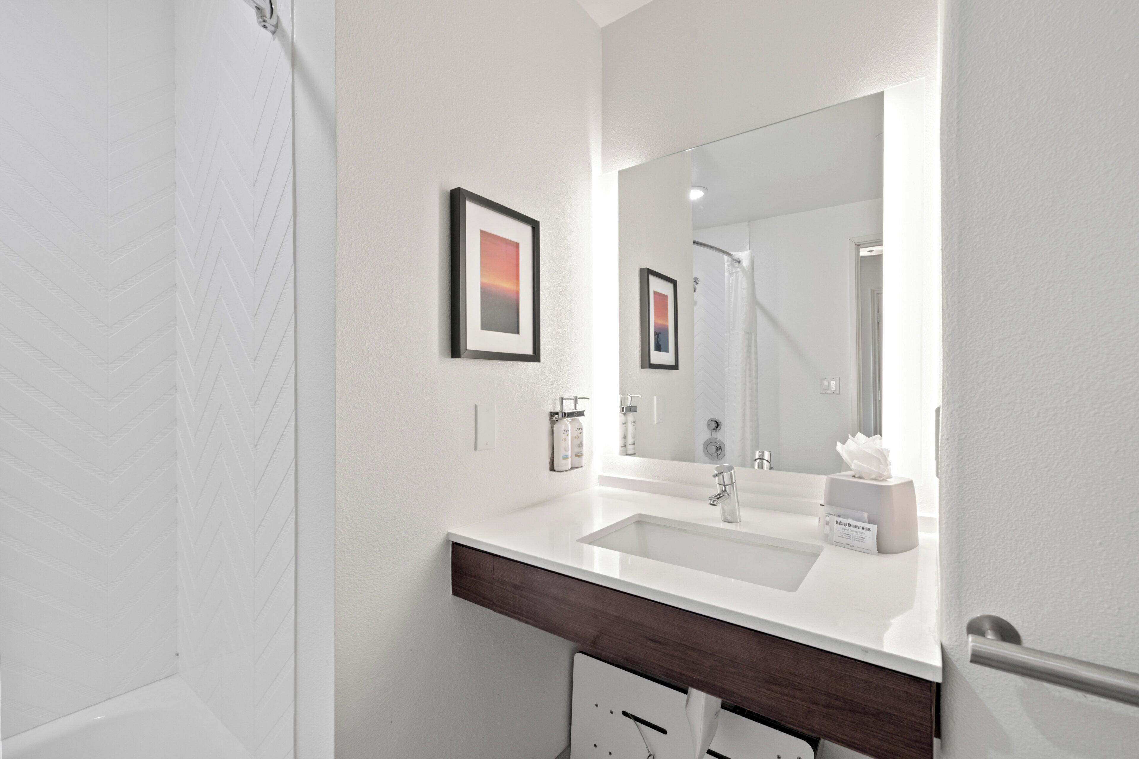 A bathroom with a white sink, a large mirror, and two framed pictures on the wall.