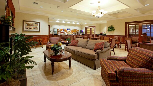A spacious lobby with a large sofa, armchairs, and a coffee table. There are several dining tables and chairs, and a chandelier hangs from the ceiling.