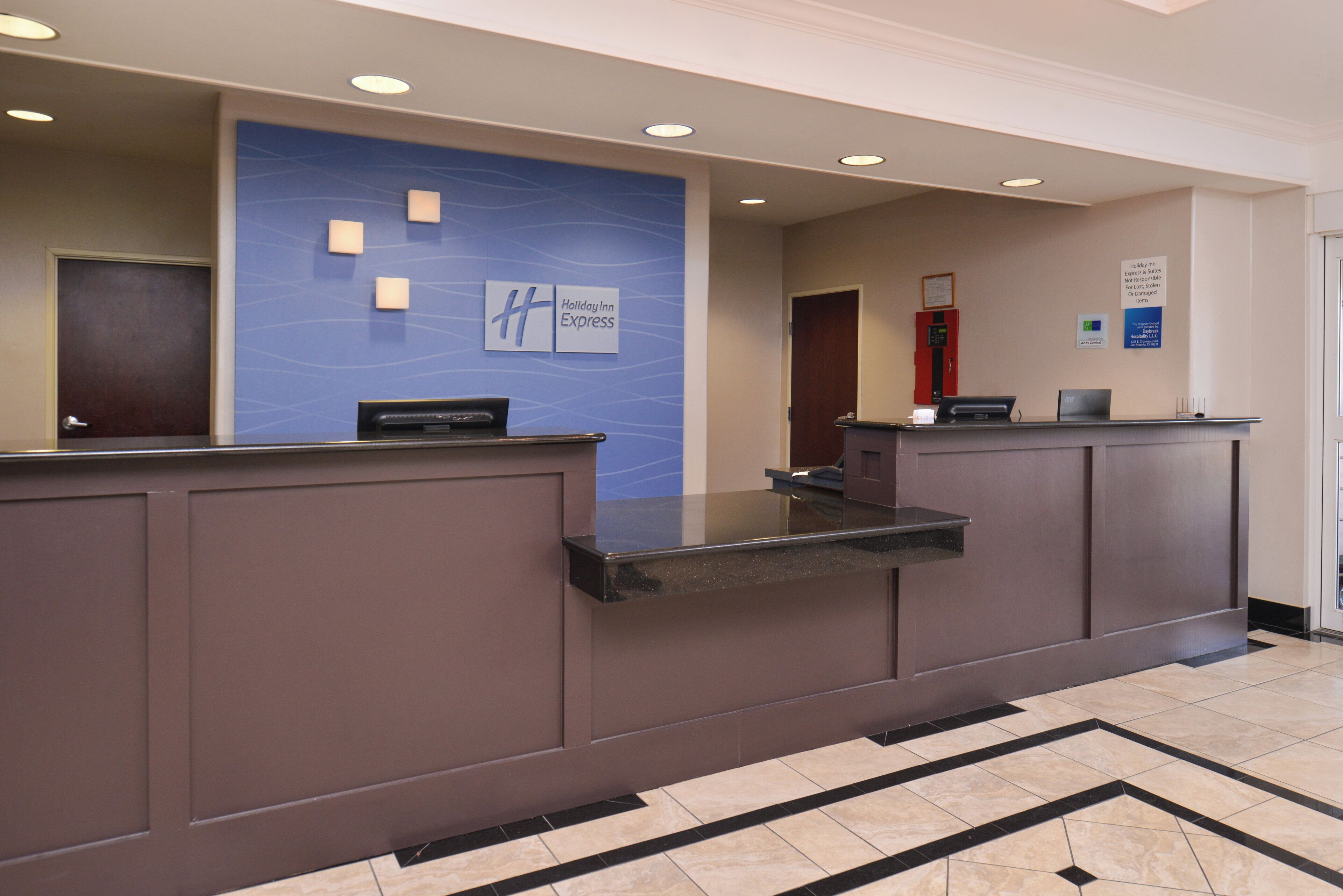 A hotel reception desk with a blue accent wall, a digital screen, and a fire alarm.