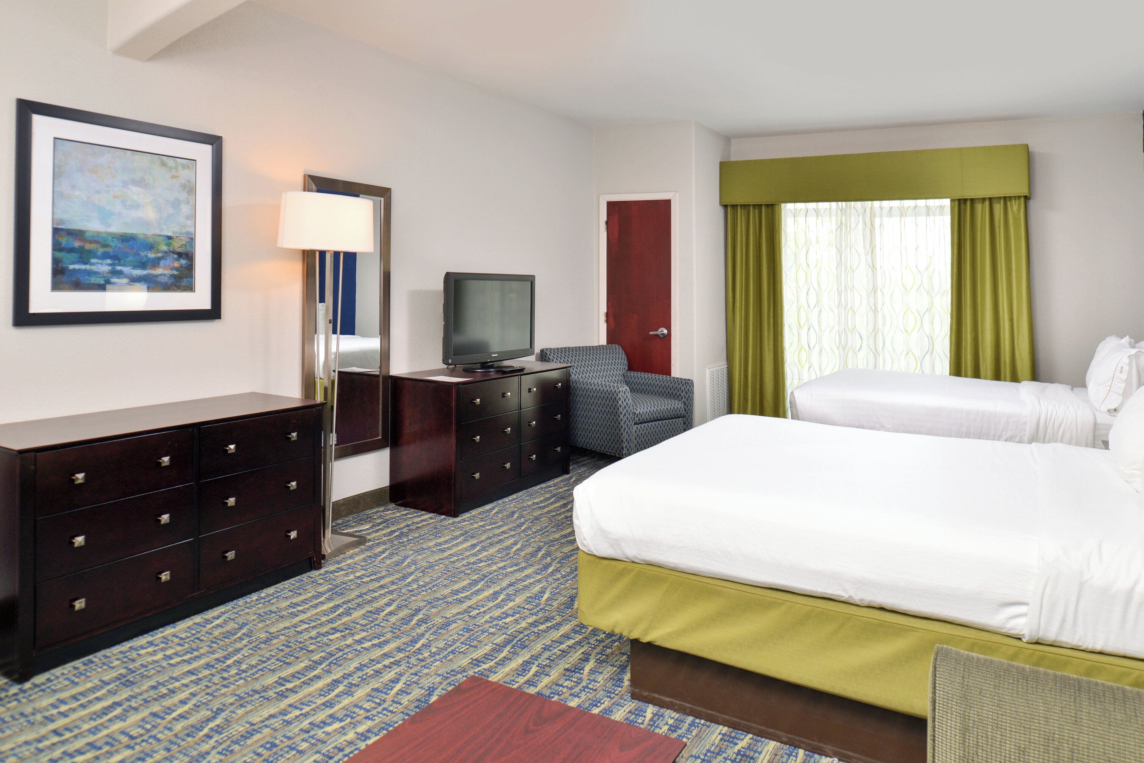 A hotel room with a bed, a television, a dresser, a chair, and a painting on the wall.