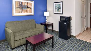 A hotel room with a green sofa, a wooden table, a lamp, a microwave, and two framed pictures on the wall.