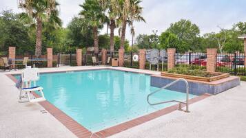 A swimming pool with a lifeguard chair, palm trees, and a brick fence.