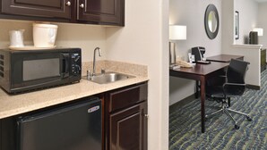 A kitchenette with a microwave, sink, and refrigerator. There is a table with a chair and a lamp in the adjacent room. - Holiday Inn Express Hotel & Suites San Antonio by IHG (San Antonio)