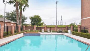 Una piscina rectangular con borde de azulejos, rodeada por un muro de ladrillo y una valla metálica.