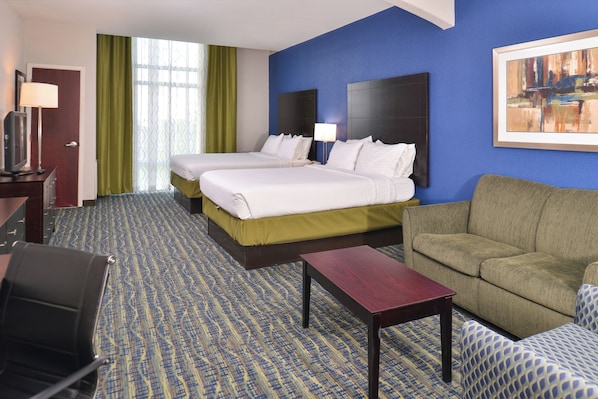 Quarto de hotel com duas camas, um sofá, uma mesa de trabalho e uma televisão.