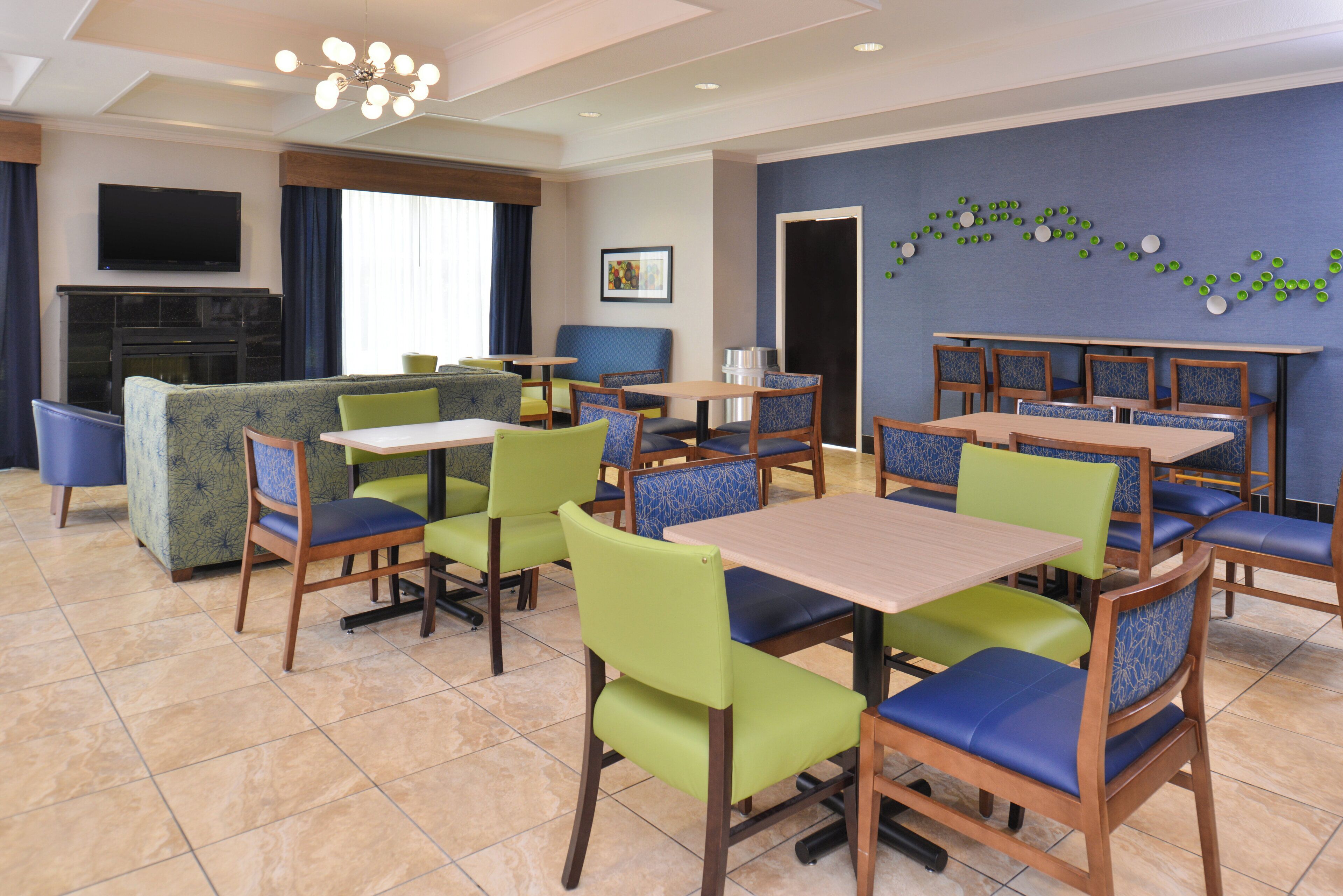 A hotel dining area with multiple tables and chairs, a television, and a fireplace.