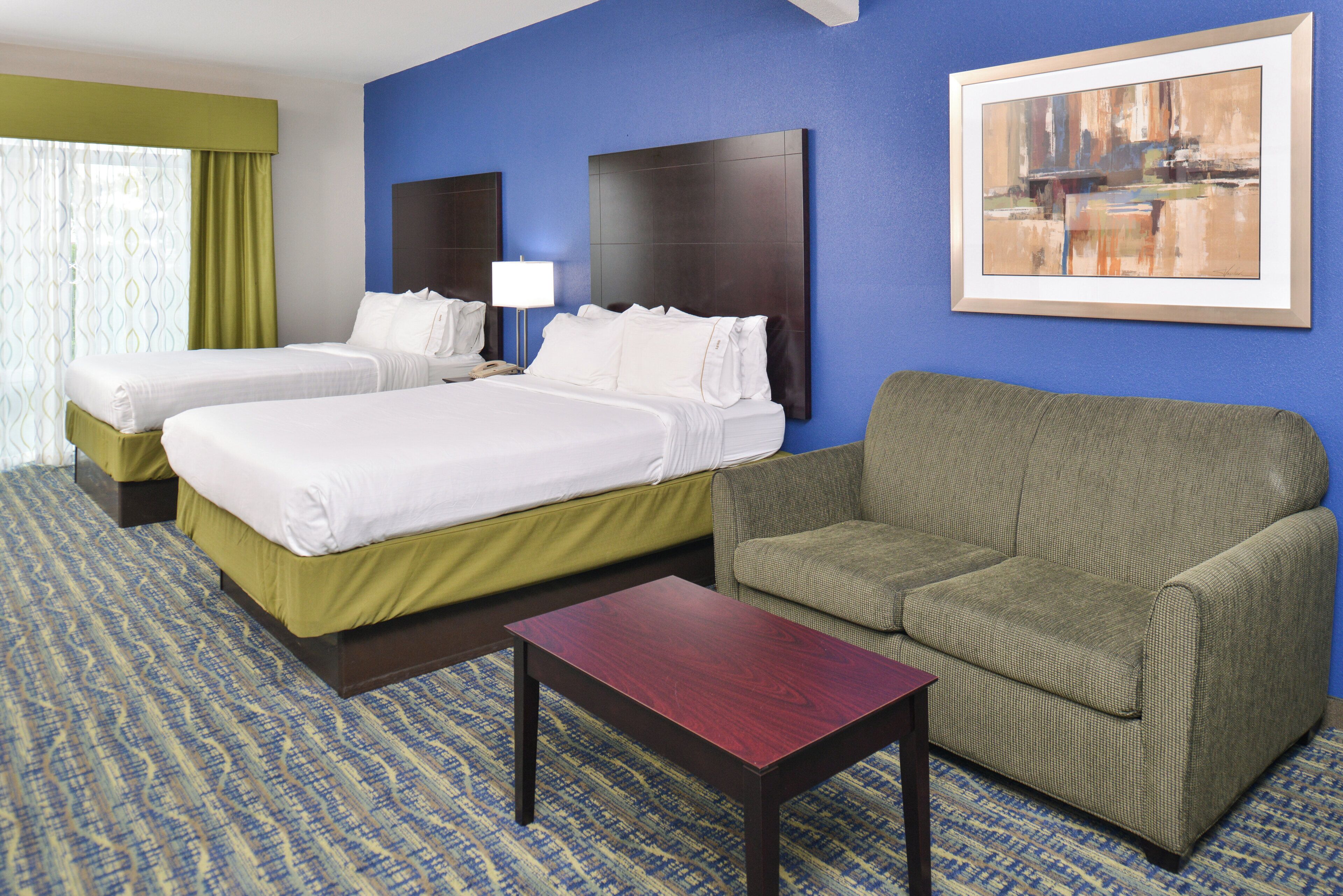 A hotel room with two beds, a sofa, a small table, and a painting on the wall.