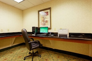 Quarto de hotel com secretária, computador, impressora e um quadro na parede.