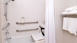 A bathroom with a bathtub, grab bars, a showerhead, and a towel rack. - Holiday Inn Express Hotel & Suites San Antonio by IHG (San Antonio)