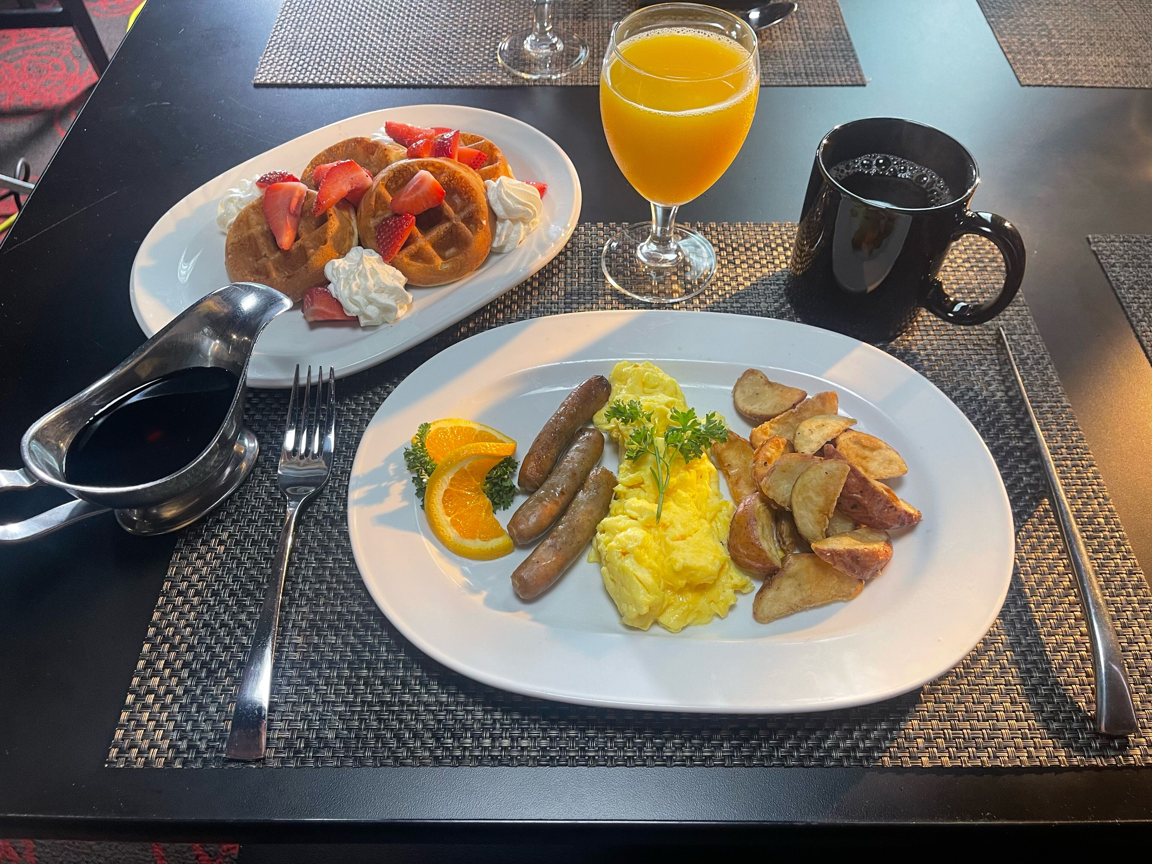 Een ontbijttafel met wafel, roerei, worst en aardappelen.