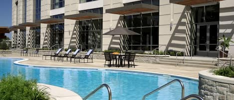 A hotel with a swimming pool, sun loungers, and outdoor seating.