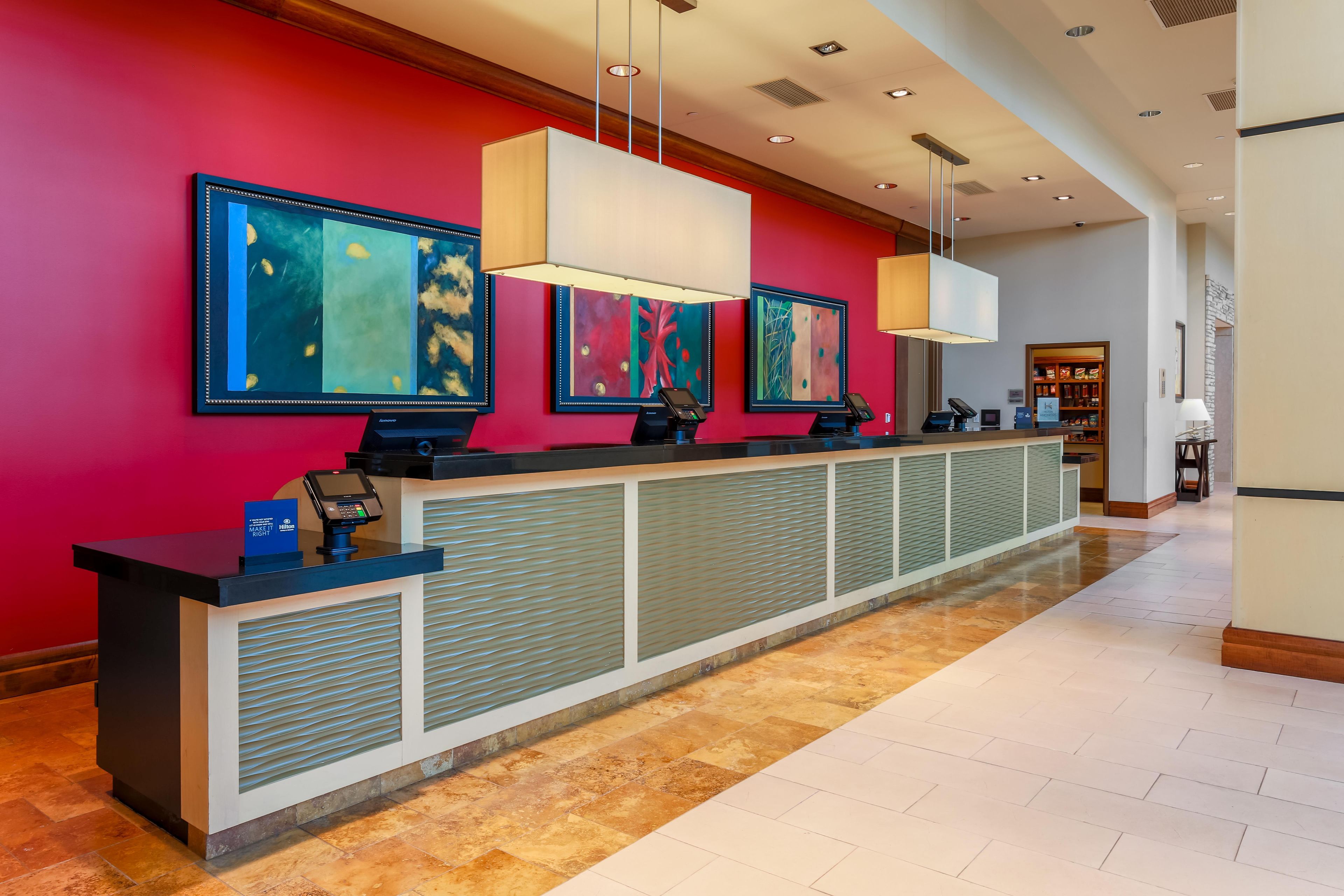 Un mostrador de recepción de hotel con diseño moderno, que presenta una pared roja, múltiples monitores y una zona de registro.