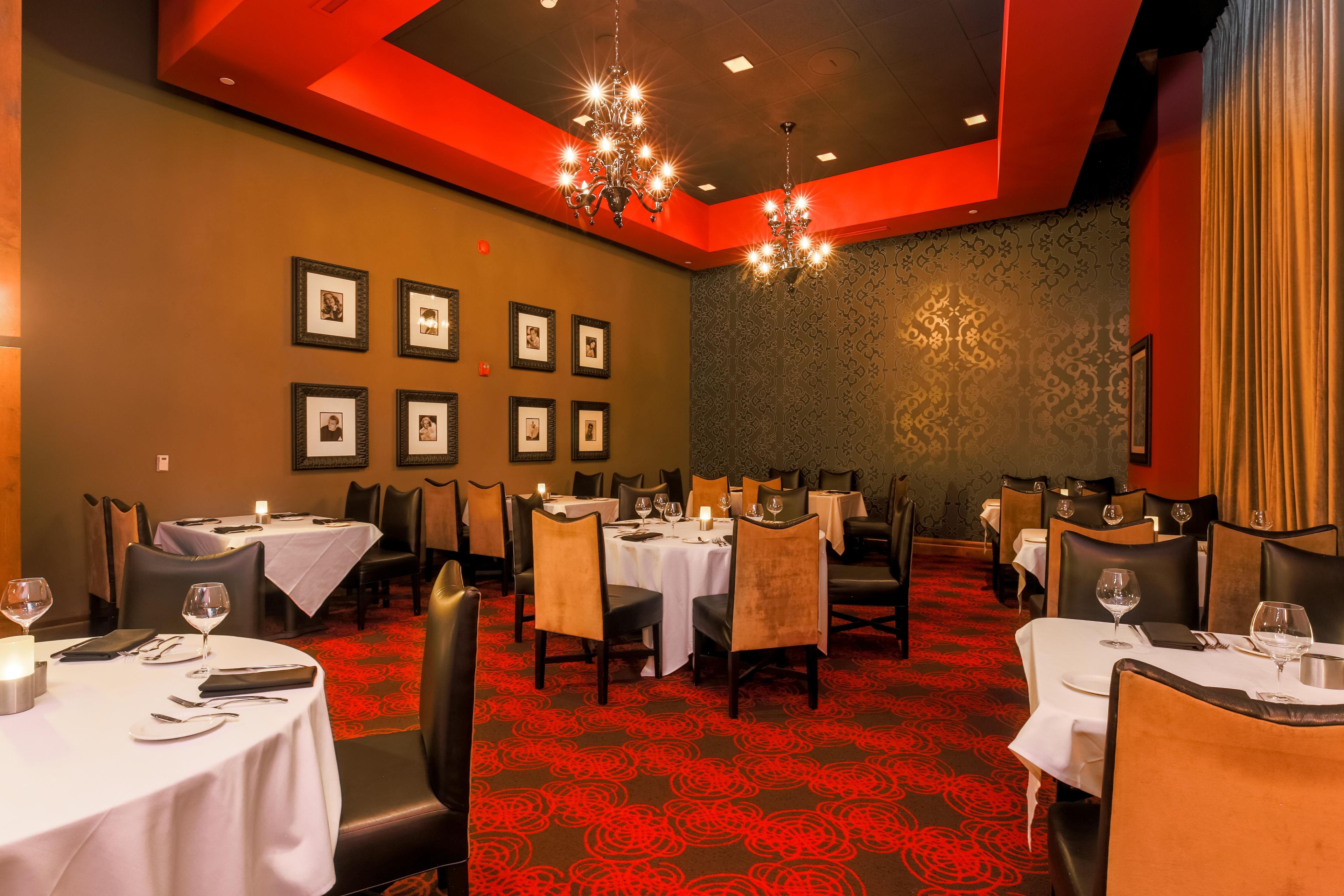 A restaurant with multiple tables and chairs, framed pictures on the wall, and a chandelier.