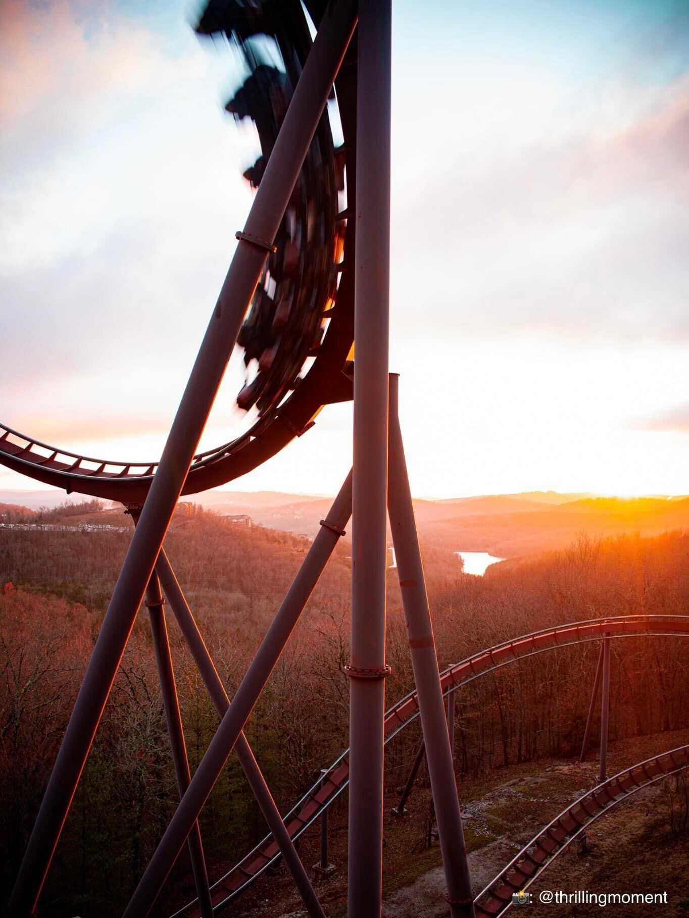 A roller coaster track with a scenic view of a forest and a body of water during sunset.