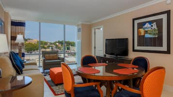 Une chambre d’hôtel comprenant un coin repas, un canapé, une télévision et une grande fenêtre donnant sur la ville.