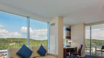 A hotel room with a large window, a sofa, a desk, and a chair.
