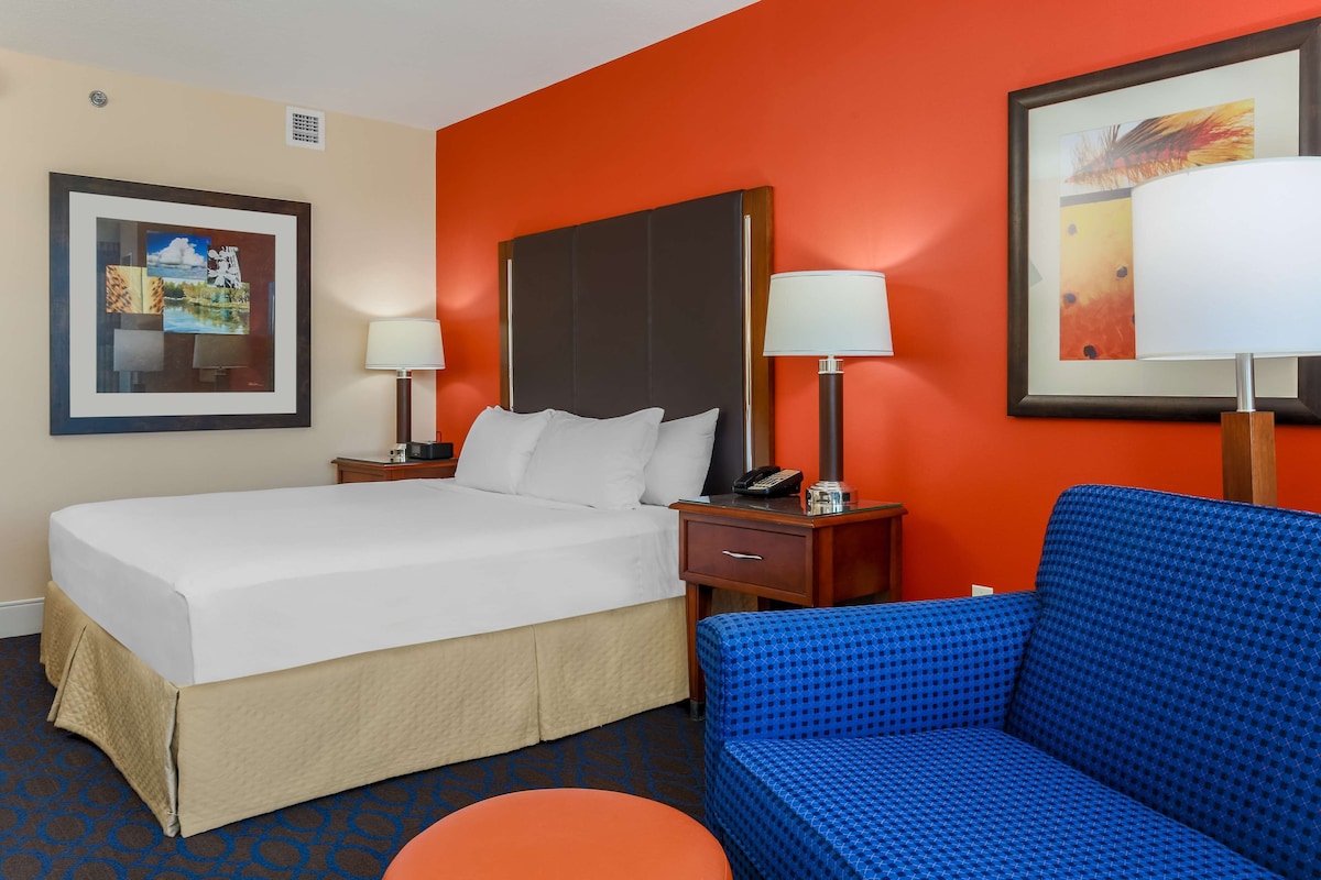 A hotel room with a bed, two bedside tables with lamps, a blue sofa, and a framed picture on the wall.