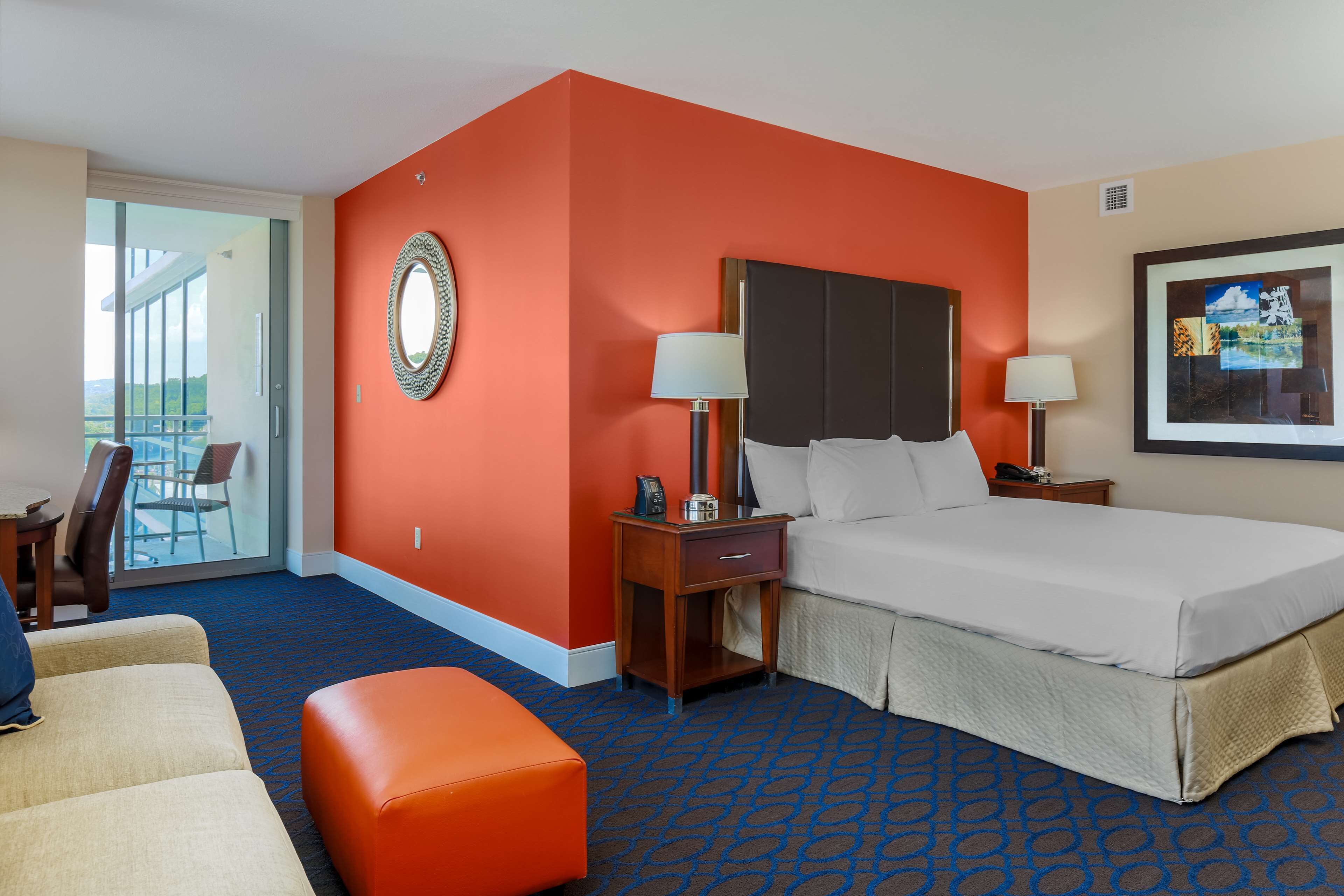 A hotel room with a large bed, two bedside tables with lamps, a chair, and a sofa.