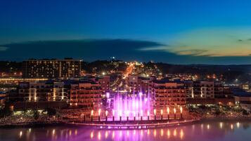 A nighttime cityscape with a fountain in the foreground and buildings in the background.