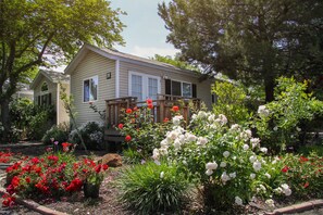 A two-story house with a front porch, surrounded by a garden with various flowering plants and shrubs. - Arden Acres Executive Suites and Cottages (Sacramento)