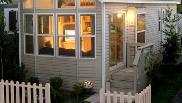 Ett litet, envåningshus med ett stort fönster mot framsidan, en liten veranda och ett vitt staket.