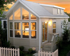 A small, single-story house with a large front window, a small porch, and a white picket fence. - Arden Acres Executive Suites and Cottages (Sacramento)