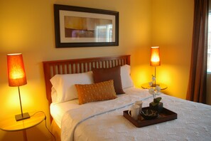 A hotel room with a bed, two bedside lamps, a tray with a cup and a bowl, and a framed picture on the wall. - Arden Acres Executive Suites and Cottages (Sacramento)